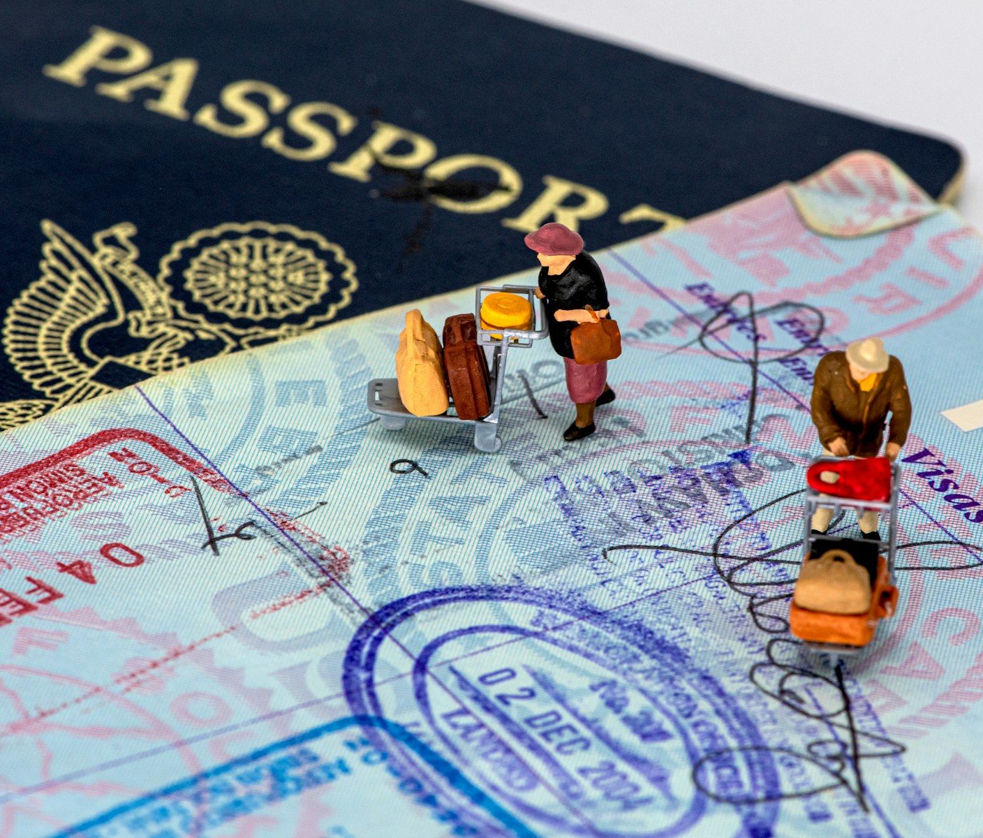 Photo by mana5280 Two miniature figures with luggage carts on a passport page with travel stamps